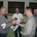 Mężczyzna w jasnej koszuli i jeansach przekazuje dyplom i statułetkę lauratowi konkursu.