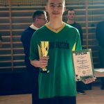 Nastolatek w stoju piłkarskim trzymajacy dyplom i puchar.