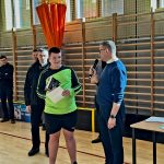 Grupa dorosłych mężczyzn z młodym zawodnikiem trzymajacym dyplom.