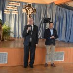 Dwóch stojących mężczyzn w garniturach. Jeden z nich przemawia przez mikrofon