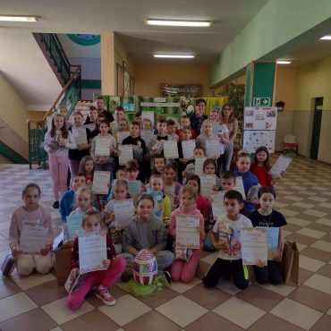 Grpa dzieci i nauczyciele na korytarzu w szkole pozują do zdjecia z dyplomami.