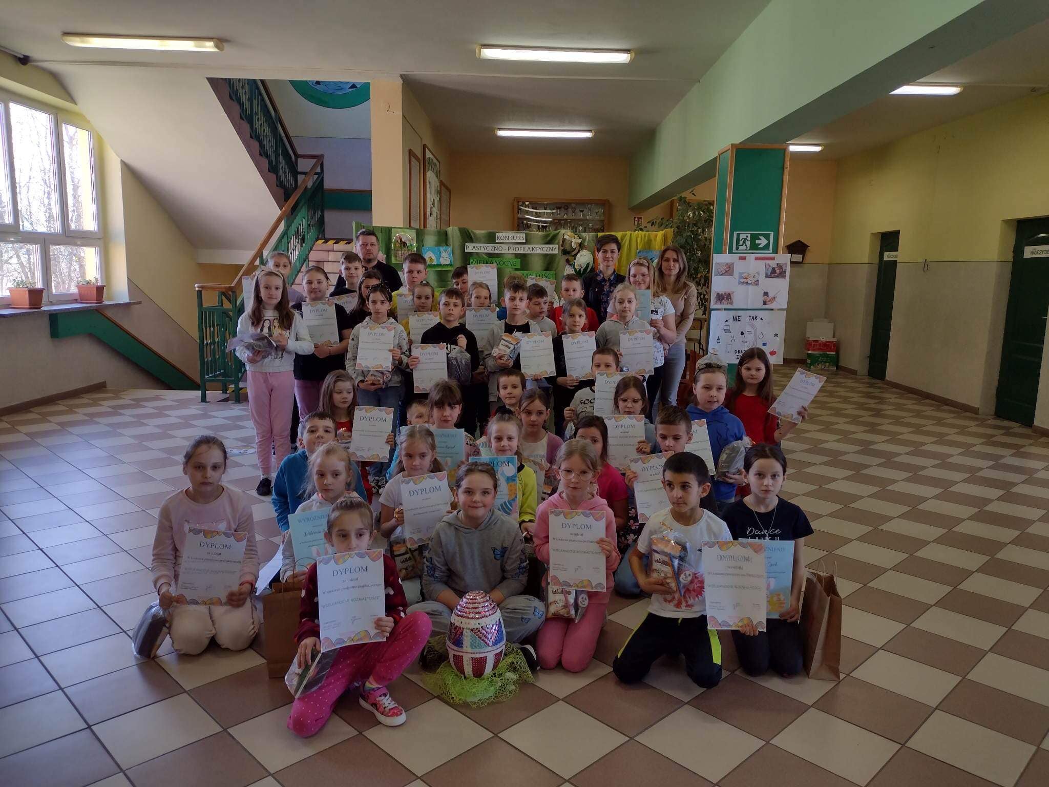 Grpa dzieci i nauczyciele na korytarzu w szkole pozują do zdjecia z dyplomami.