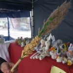 Ozdoby na kiermaszu wielkanocnym zaprezentowane na stole i palma na pierwszym planie.