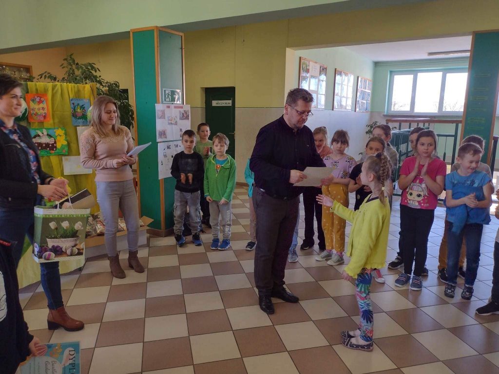 Grupa dorosłych wręcza dyplomy dzieciom w szkole na korytarzu.