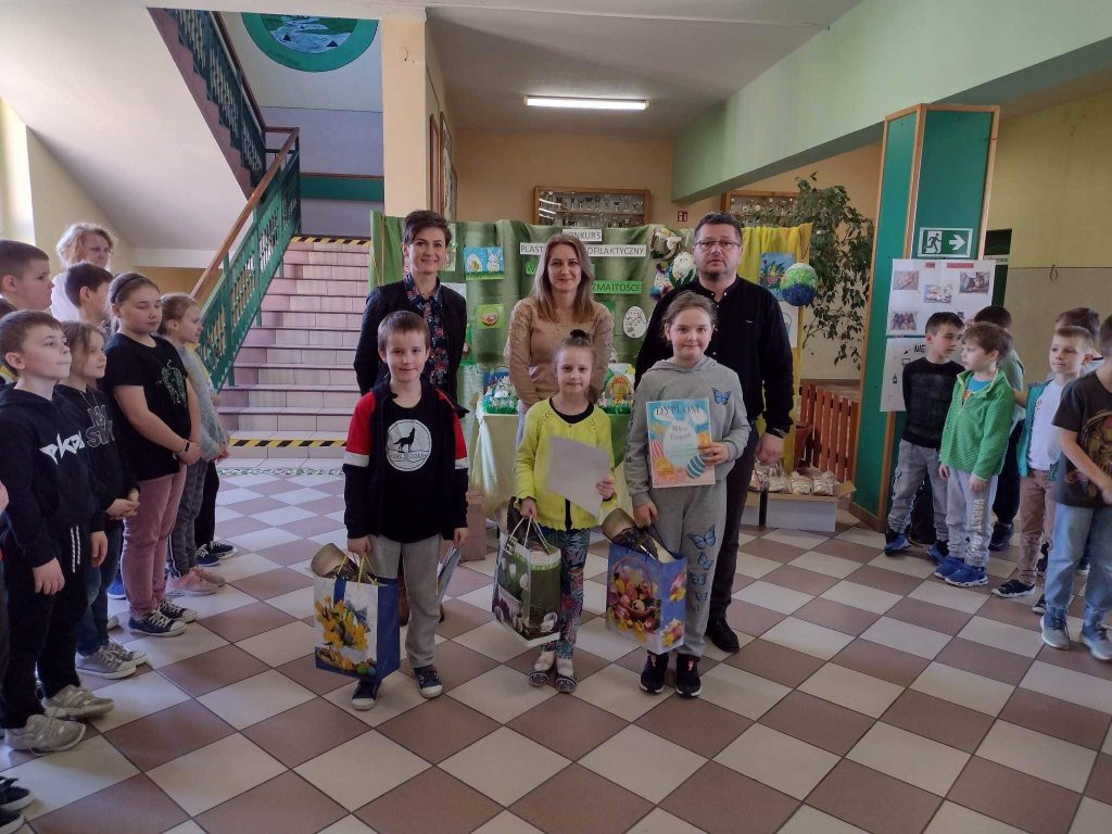 Grpa dzieci i nauczyciele na korytarzu w szkole pozują do zdjecia z dyplomami i podarunkami..