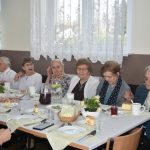 Grup kobiet zasiadajaca na sali przy zastawionych stołach.