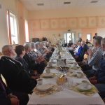 Duża grupa osób róznej płci i wieku zasiadajaca przy stołach na sali.