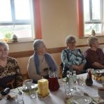 Grupa kobiet zasiadajaca na sali przy zastawionych stołach.