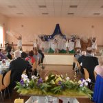 Grupa dzieci ubranych w odswietne stoje na scenie. Ogląda je duża grupa osób róznej płci i wieku.