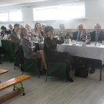 Grupa dorosłych zasiadajacych przy podłuznym stole na sali.