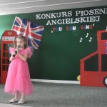 Dziewczynka w różowej sukni śpiewajaca na sali podczas przedstawienia.