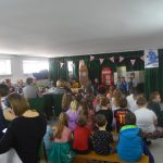 Dorosli i dzieci ogladający przestawienie arystyczne przedszkolaków na sali.