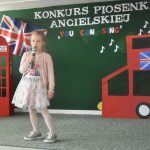 Dziewczynka w jasnej sukience śpiewajaca na sali podczas przedstawienia.