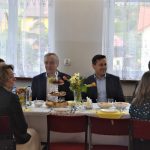 Trzech mężczyzn w garniturach i trzy kobiety siedzące przy zastawionym stole.