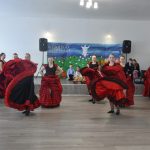 Grupa młodych dziewcząt w czarno-czerwonych sukniach w czasie wystepu tanecznego na sali.