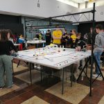 Grupa młodzieży przy dużym białym stole z przeszkodami.