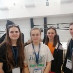 Grupa trzech dziewcząt i młody męczyzna pozujacy do zdjęcia na rozległej sali..