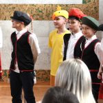 Grupa dzieci w odświetnych strojach na sali gimanstycznej w czasie przedstawienia wielkanocnego.