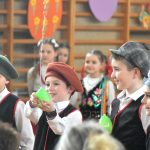 Grupa dzieci w odświetnych strojach na sali gimanstycznej w czasie przedstawienia wielkanocnego.