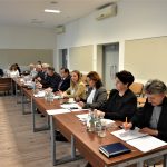 Grupa dorosłych osób w oficjalnych strojach siedzacych na sali obrad przy biurkach.