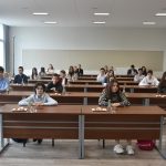 Grupa młodzieży siedzaca za biurkami w sali konferencyjnej.