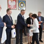 Grupa dorosłych mężczyzn i kobiet wręczają upominki młodemu chłopakowi na sali gimanstycznej.