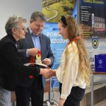 Mężczyzna i kobieta wręczają upominki młodej dziewczynie na sali gimanstycznej.