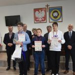 Grupa trzech młodych chłopców z dyplomami i grupa dorosłych na sali konferencyjnej..