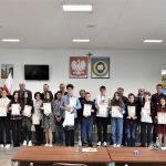 Duża grupa młodzieży z dyplomami i grupa dorosłych na sali konferencyjnej.