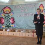 Kobieta w odświętnym ciemnym stroju przemawia za pomocą mikrofonu.