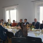 Duża grupa osób róznej płci i wieku zasiadajaca przy stołach na sali.