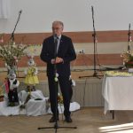 Starszy mężczyzna w garniturze przemawia za pomocą mikrofonu na sali.