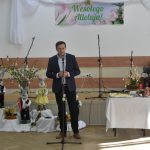 Młody mężczyzna w garniturze przemawia za pomocą mikrofonu na sali.