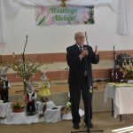 Starszy mężczyzna w garniturze przemawia za pomocą mikrofonu na sali.