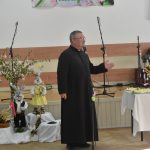 Starszy mężczyzna w sułtannie przemawia za pomocą mikrofonu na sali.