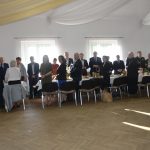 Grupa osób stojąca przy stołach na sali.