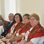 Grupa kobiet i meżczyzn siedzaca przy zastawionym stole na sali.