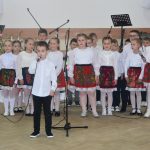 Grupa dzieci w odswiętnych strojach w czasie wystepu na sali.