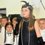 Grupa dzieci w odswiętnych strojach w czasie wystepu na sali.