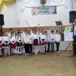 Grupa dzieci w odswiętnych strojach w czasie wystepu na sali.