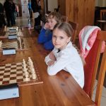 Grupa dzieci grająca w szachy w pomieszczeniu.