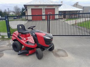 Czerwono-czarny traktorek ogrodowy na tle budynku OSP.