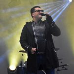 Mezczyzna w ciemnej kurtce i czrnych okularach śpiewa na scenie.