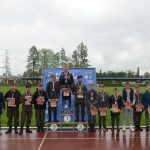 Grupa młodziezy i dorosłych pozujaca do zdjecia na stadionie. Młodzież ma dyplomy i medale.