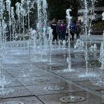 Grupa dzieci stojąca za fontanną.