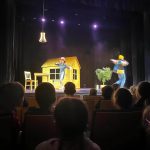 Grupa osób (przeważnie dzieci) oglądająca występ teatralny.