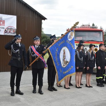 Grupa strażaków z pocztem sztandarowym na uroczystej zbiórce.