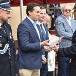 Mężczyzna w stroju strażackim wręcza upominek mężczyźnie w garniturze.