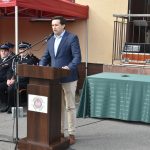 Mężczyzna w garniturze przemawia za pomocą mikrofonu przy mównicy.