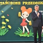 Męzczyzna w graniturze przemiawiajacy do mikrofonu.